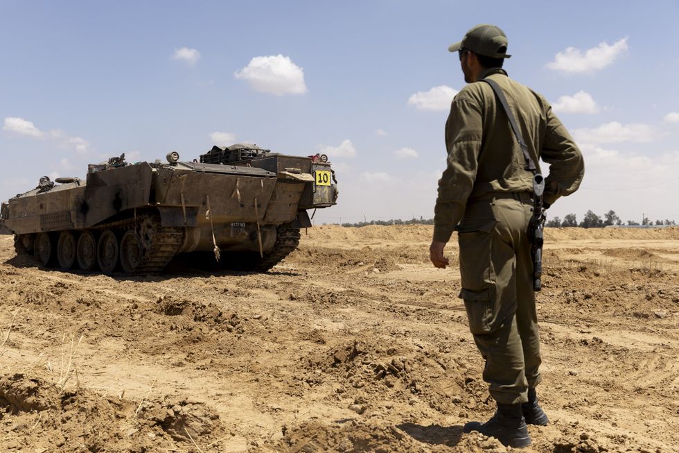 An Israeli soldier walks near an armored personnel carrier near the border with the southern Gaza Strip