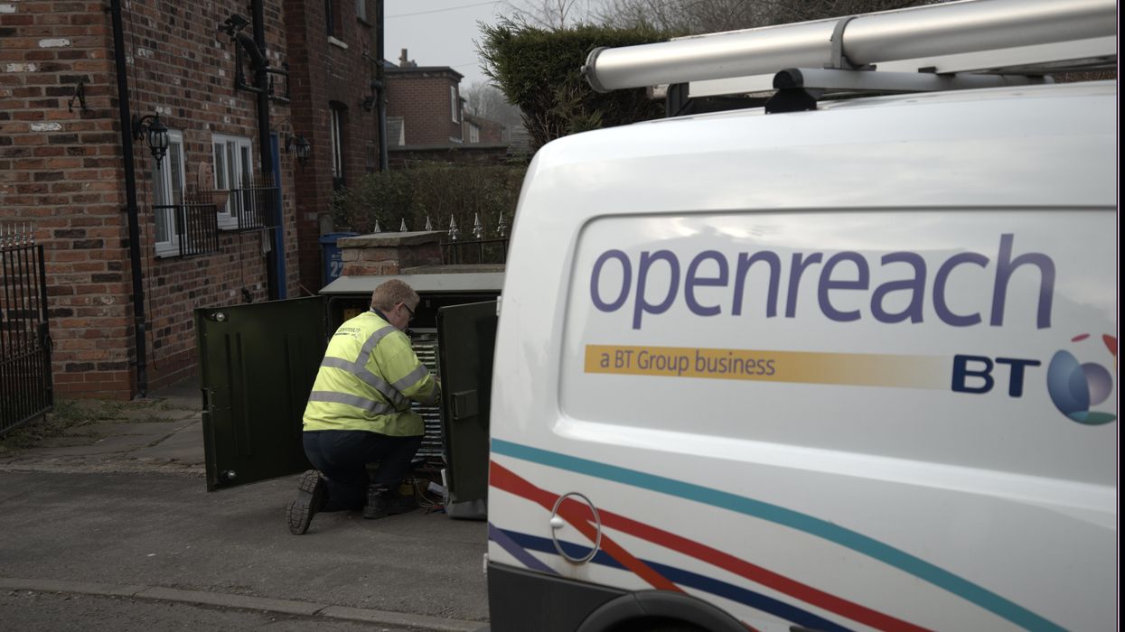an openreach engineer is pictured making adjustments inside an exchange cabinet on the streets with a BT and openreach branded van parked beside him