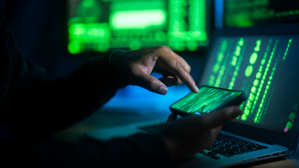 an unseen person holds a smartphone with green lines of code on-screen