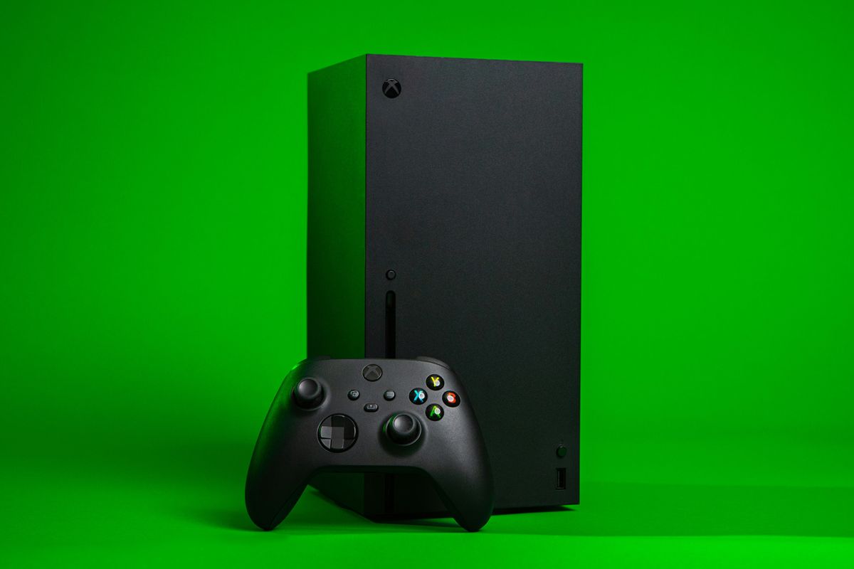 an xbox series x console is pictured against a green background with a controller leaning against it 