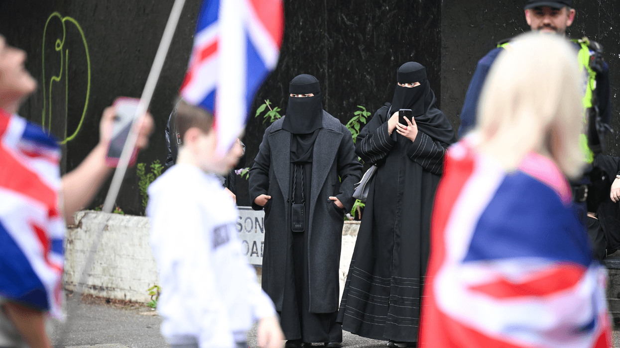 Anti-migrant protesters march past women wearing Burkas