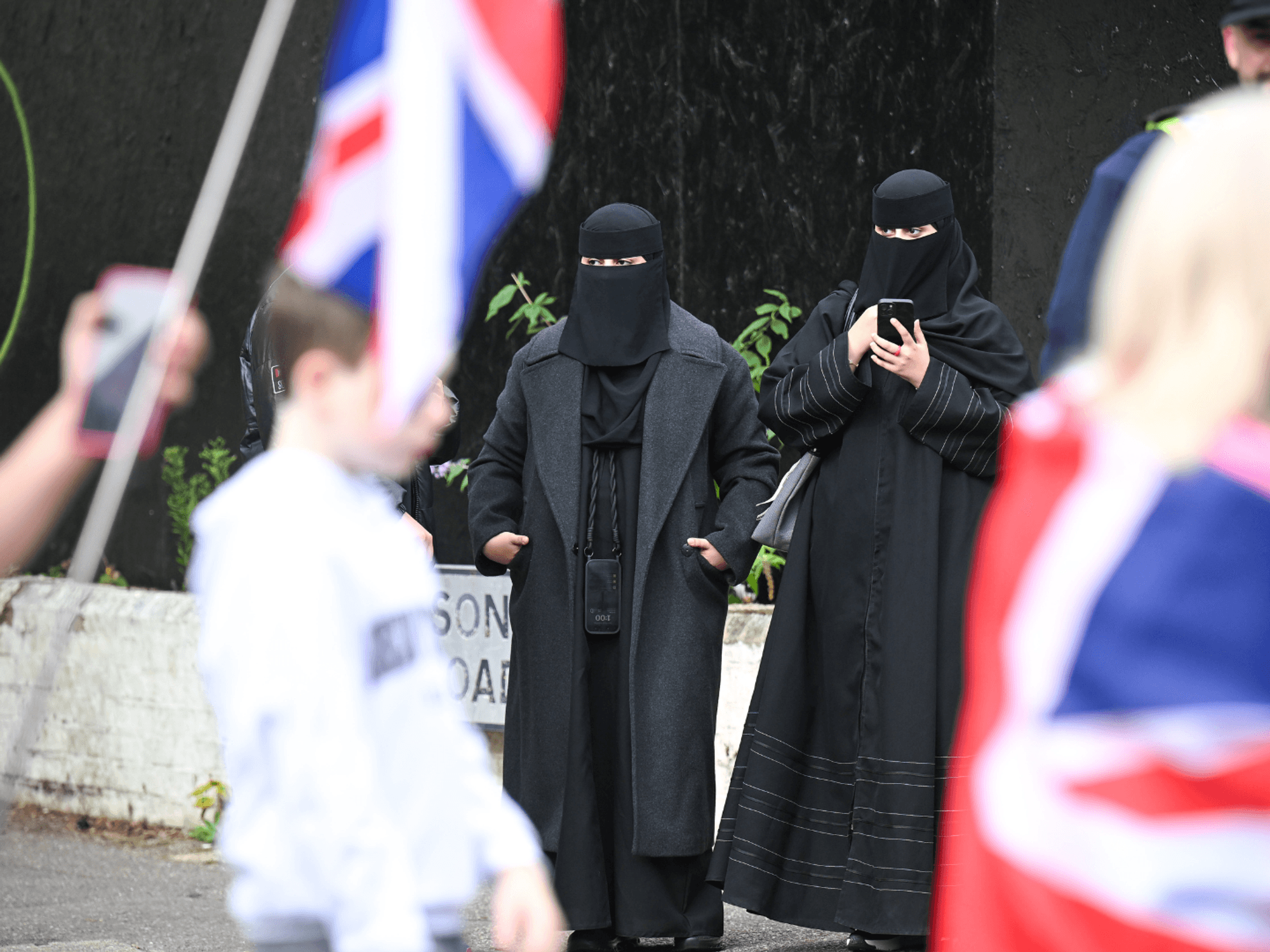 Anti-migrant protesters march past women wearing Burkas