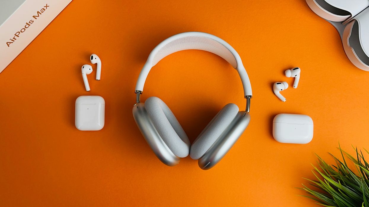 apple airpods, airpods max, and airpods pro pictured on an orange table with plants and boxes for the products