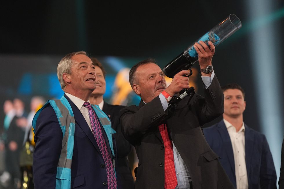 Arron Banks, Reform's mayoral candidate for the West of England, fires a Reform t-shirt in to the crowd watched by Reform UK leader Nigel Farage during the Reform UK local election launch rally at the Utilita Arena Birmingham