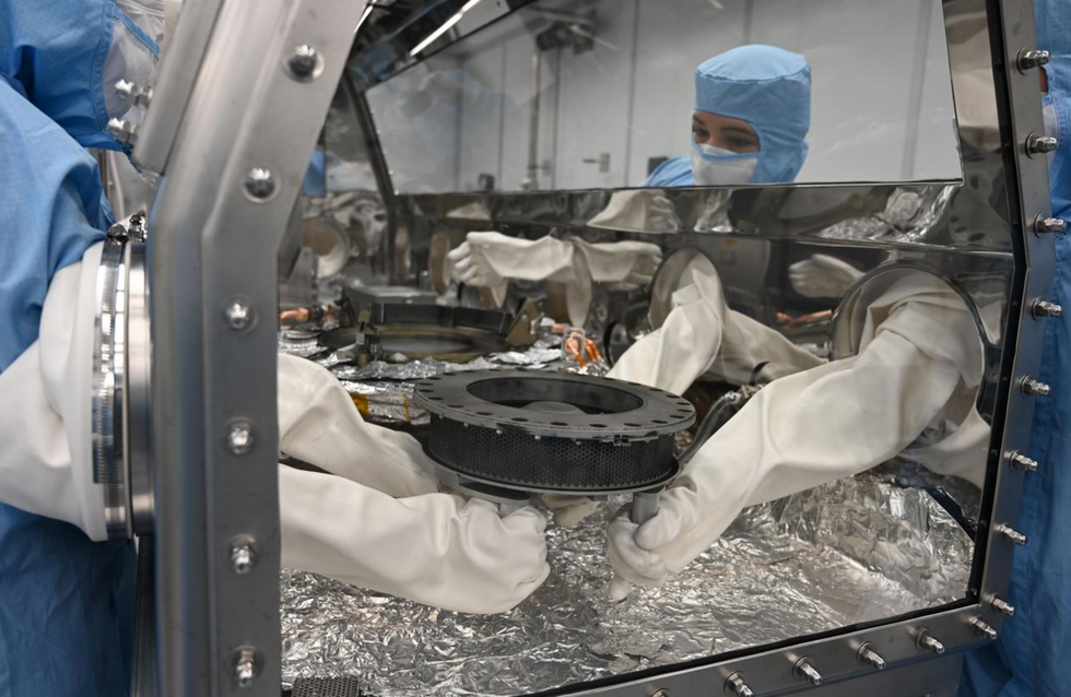 Astromaterials processor Mari Montoya and OSIRIS-REx curation team members set the TAGSAM (Touch and Go Sample Acquisition Mechanism) down in the canister glovebox after removing it from the canister base and flipping it over