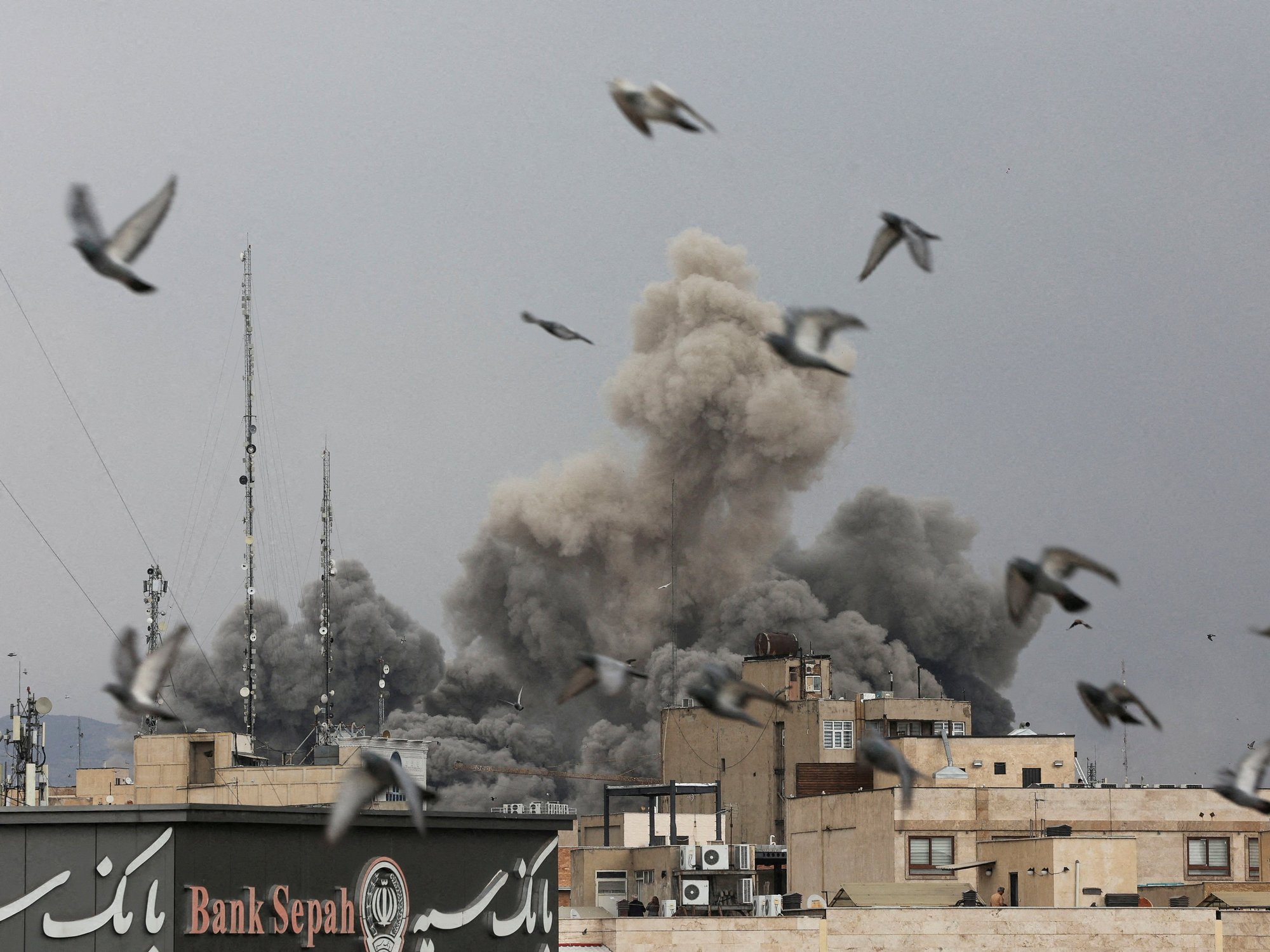 Birds fly as smoke rises following an explosion, after Israel and the U.S. launched strikes on Iran,