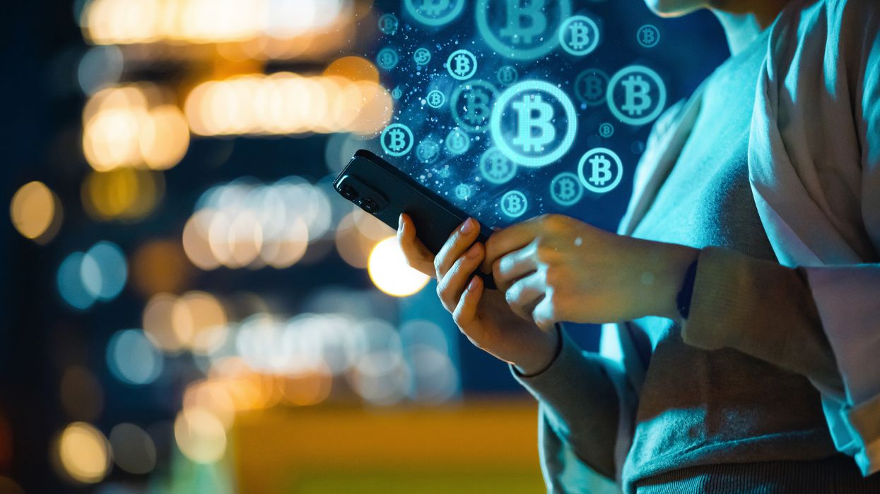 Bitcoin logo in background and person checks phone