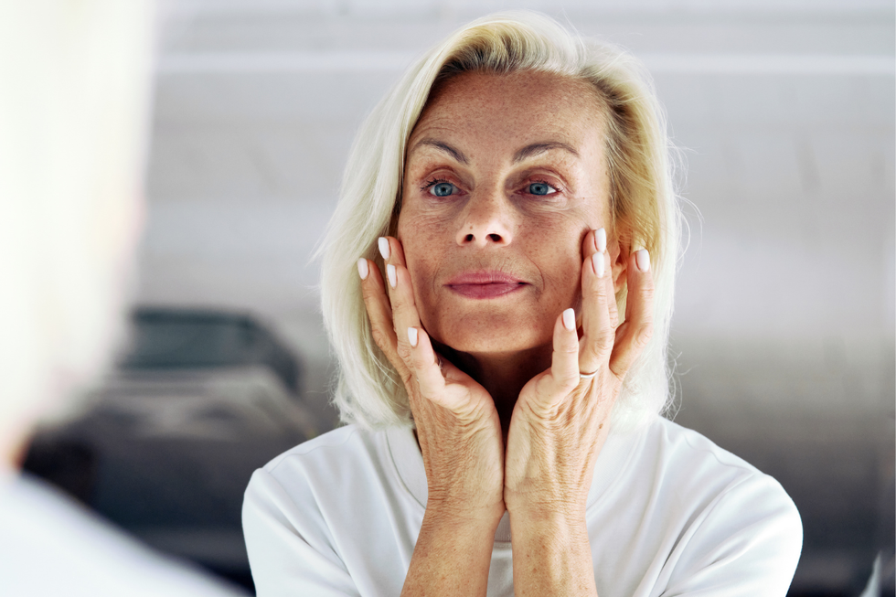 Blonde haired woman looking at her skin in the mirror