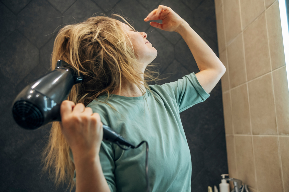 Blonde woman drying her hair in a bathroom