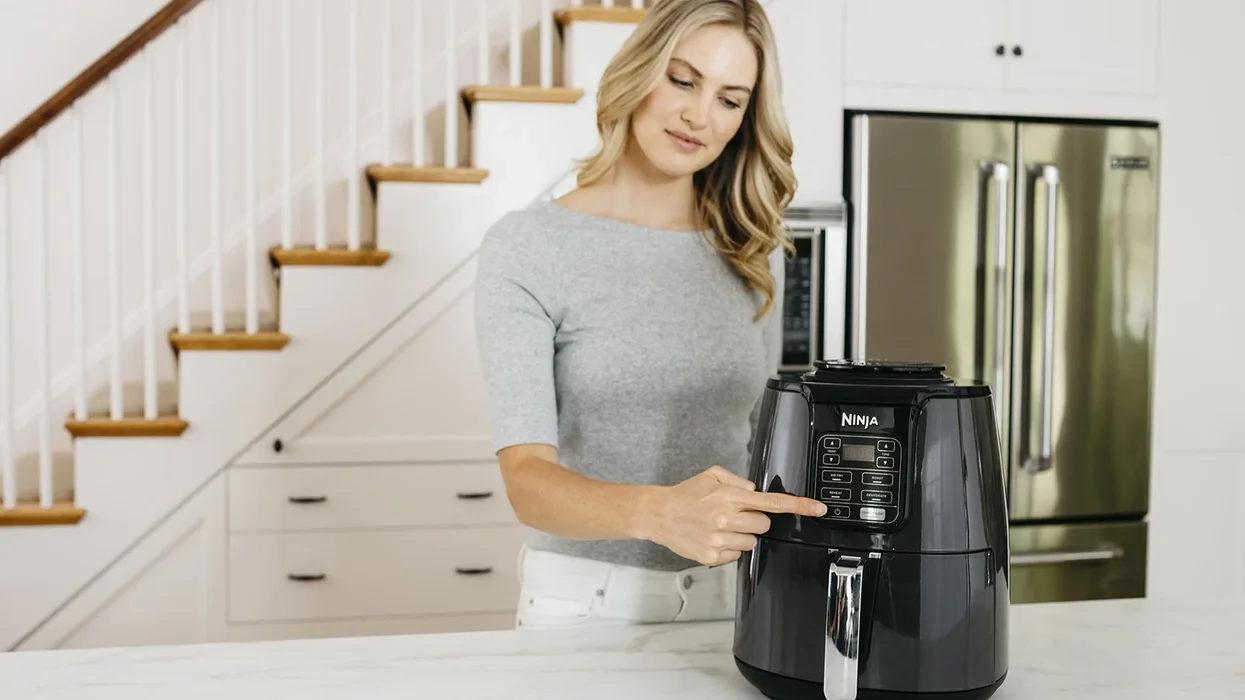 blonde woman presses a button on the front of a ninja air fryer to start cooking