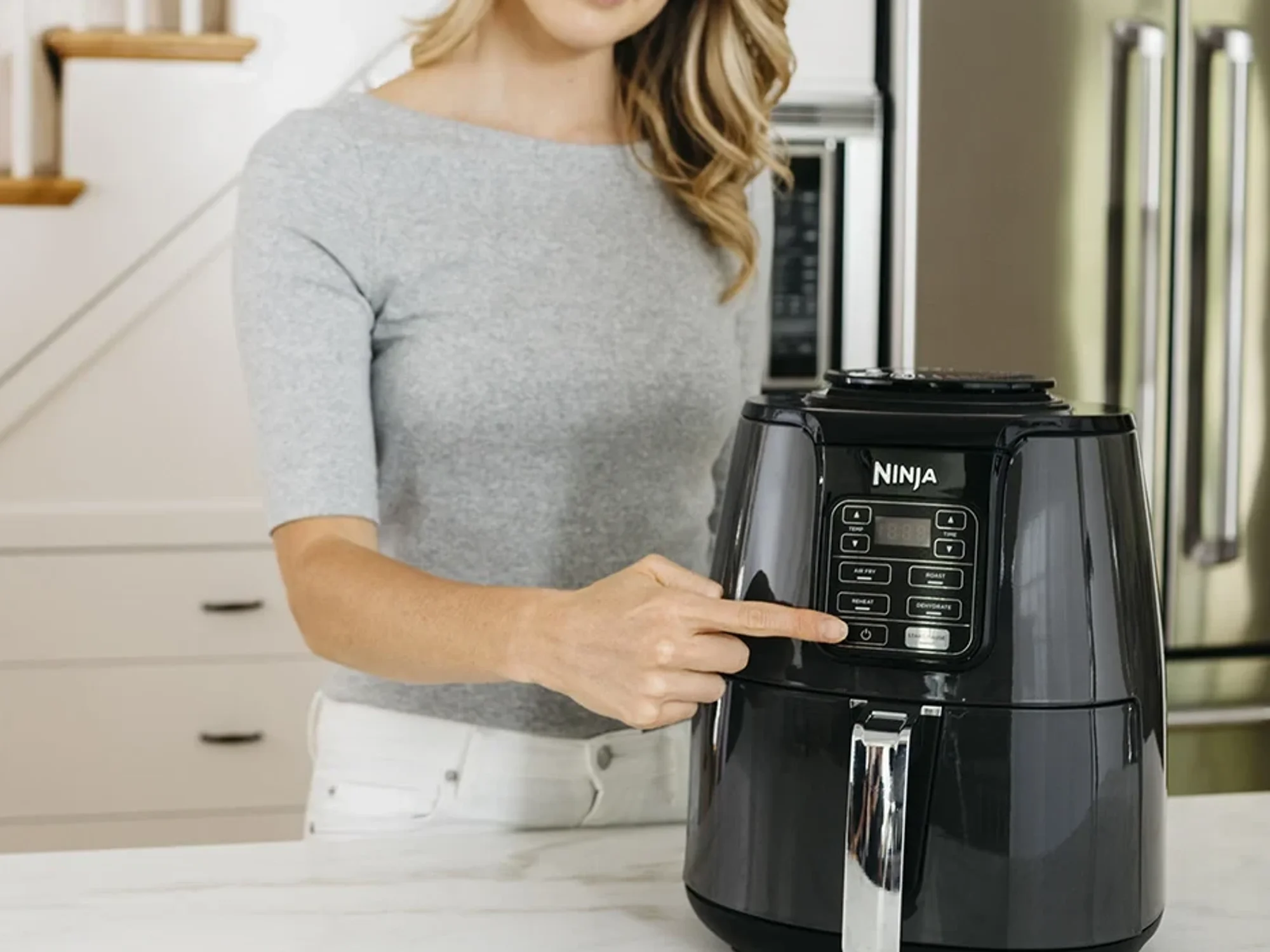 blonde woman presses a button on the front of a ninja air fryer to start cooking