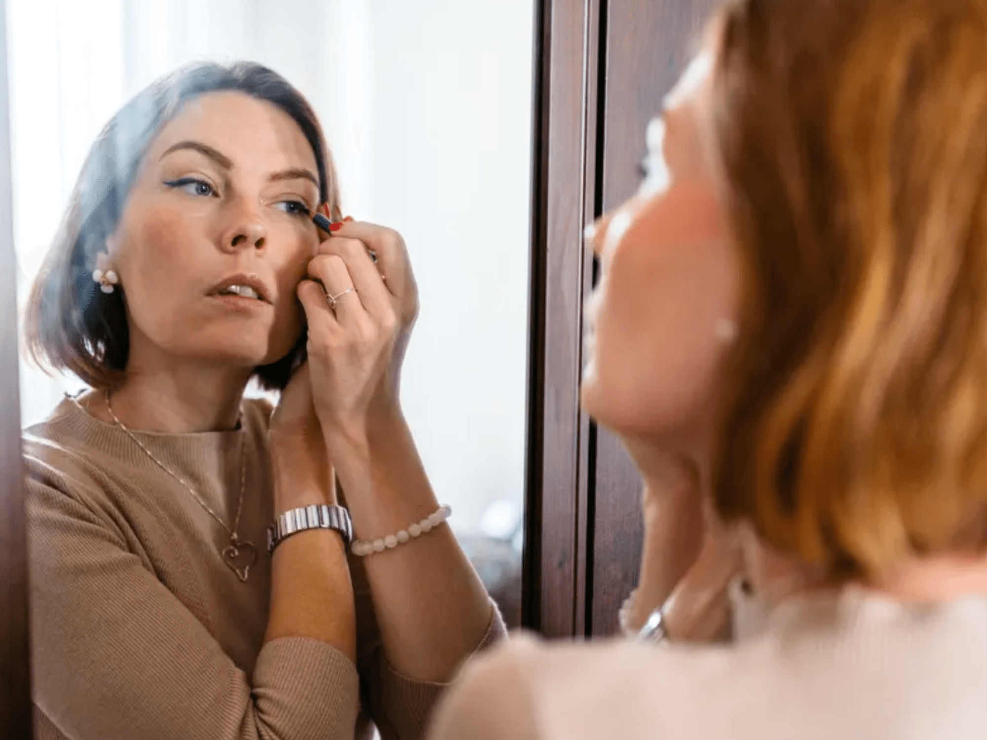 Brunette woman applying eyeliner in the mirror