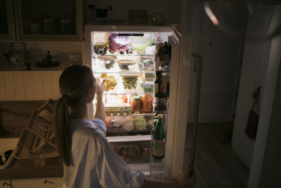 Brunette woman looking into her fridge at night