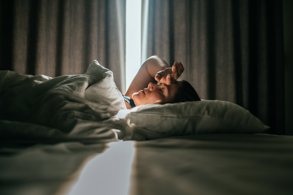 Brunette woman lying in bed in a dark room with the curtains partially open