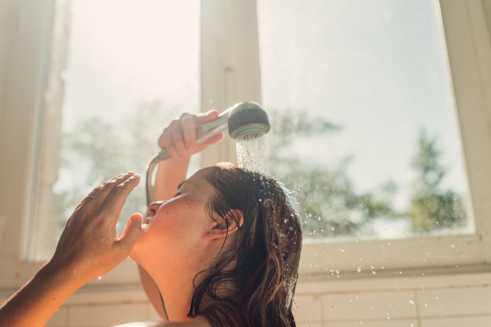 Brunette woman using a shower head to rinse her hair