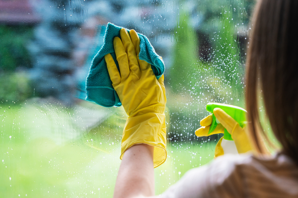 Brunette woman wearing yellow cleaning gloves to clean a window