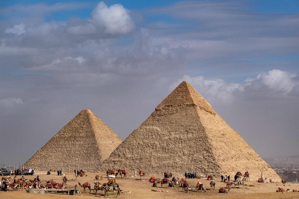 Camel guides wait with their animals near the (L) Great Pyramid of Khufu (Cheops) and the Pyramid of Khafre (Chephren) at the Giza Pyramids