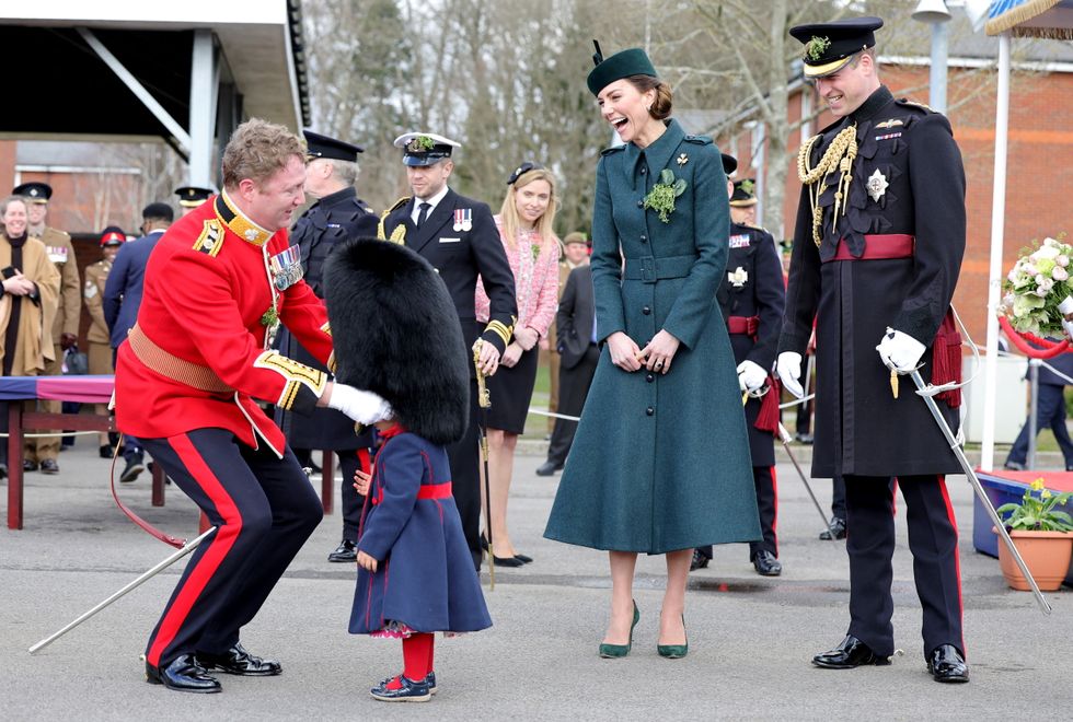 Catherine, Duchess of Cambridge and Prince William, Duke of Cambridge smile as Lieutenant Colonel Rob Money puts a bearskin hat on his 20-month-old daughter Gaia Money's head.