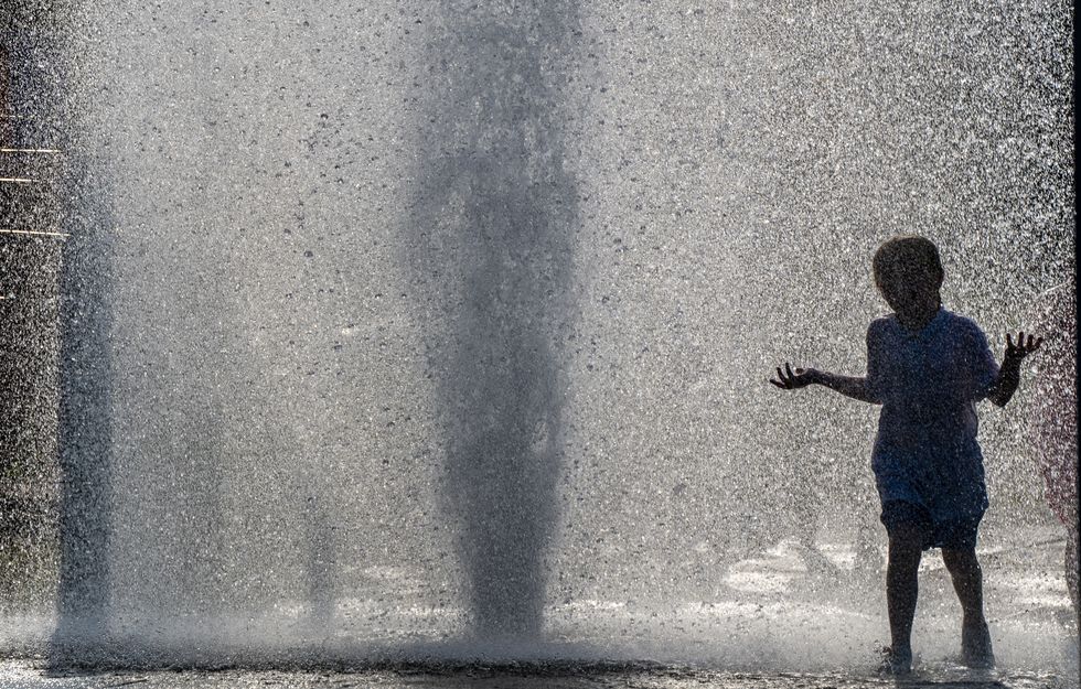 Children play in a burst water main on Harstbourne Avenue in Belle Vale, Liverpool during one of the hottest days of the year.