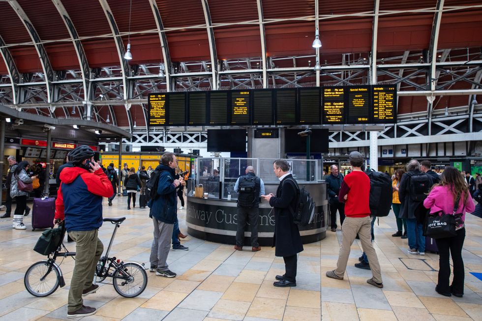 Commuters view a live departure board at Paddington rail station showing delayed and cancelled trains