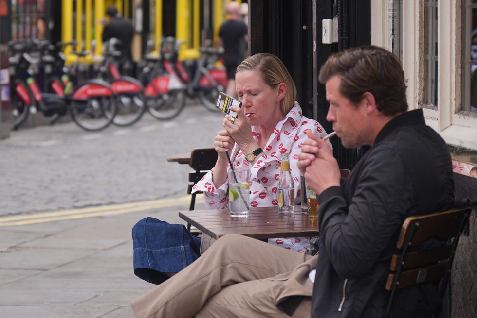 Customers light up cigarettes while sitting outdoors in a pub