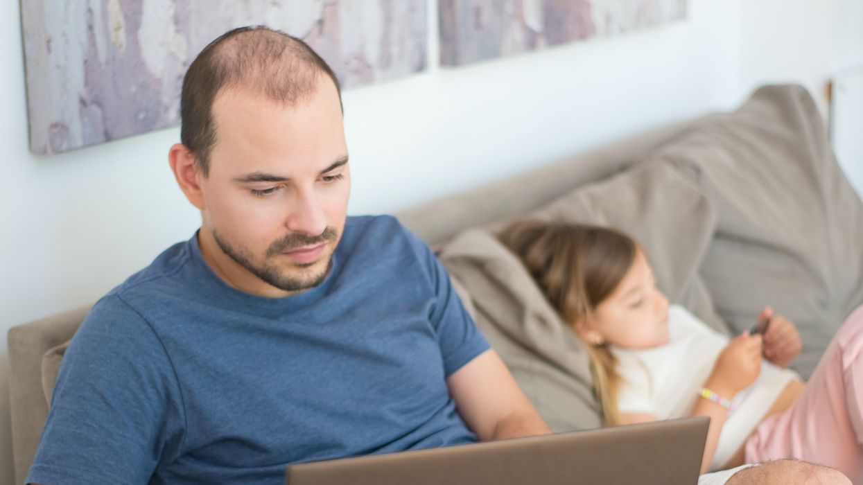 Dad looks at laptop on sofa beside child