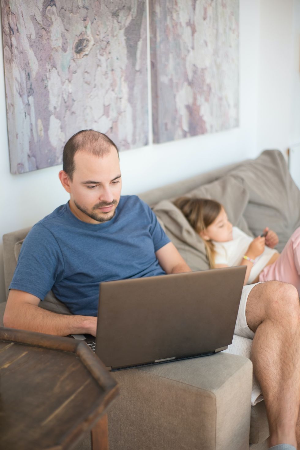 Dad looks at laptop on sofa beside child