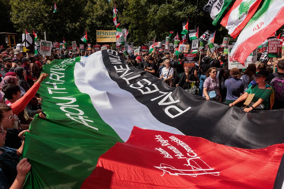 Demonstrators hold large Palestinian flag with Islamic Human Rights Commission logo on it