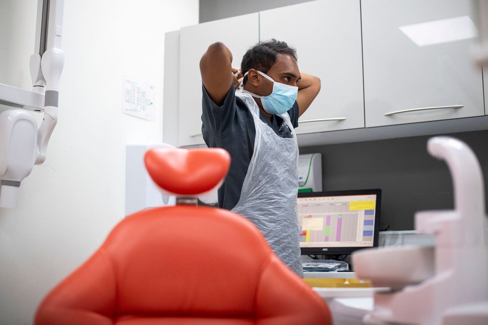 Dentist Dr Roy Woodhoo puts on PPE before treating a patient at Woodford Dental Care