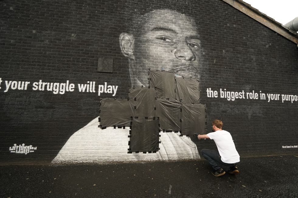 Ed Wellard, from Withington, tapes bin liners across offensive wording on the mural of Manchester United striker and England player Marcus Rashford on the wall of the Coffee House Cafe on Copson Street, Withington, which appeared vandalised the morning after the England football team lost the UEFA Euro 2021 final. Picture date: Monday July 12, 2021.