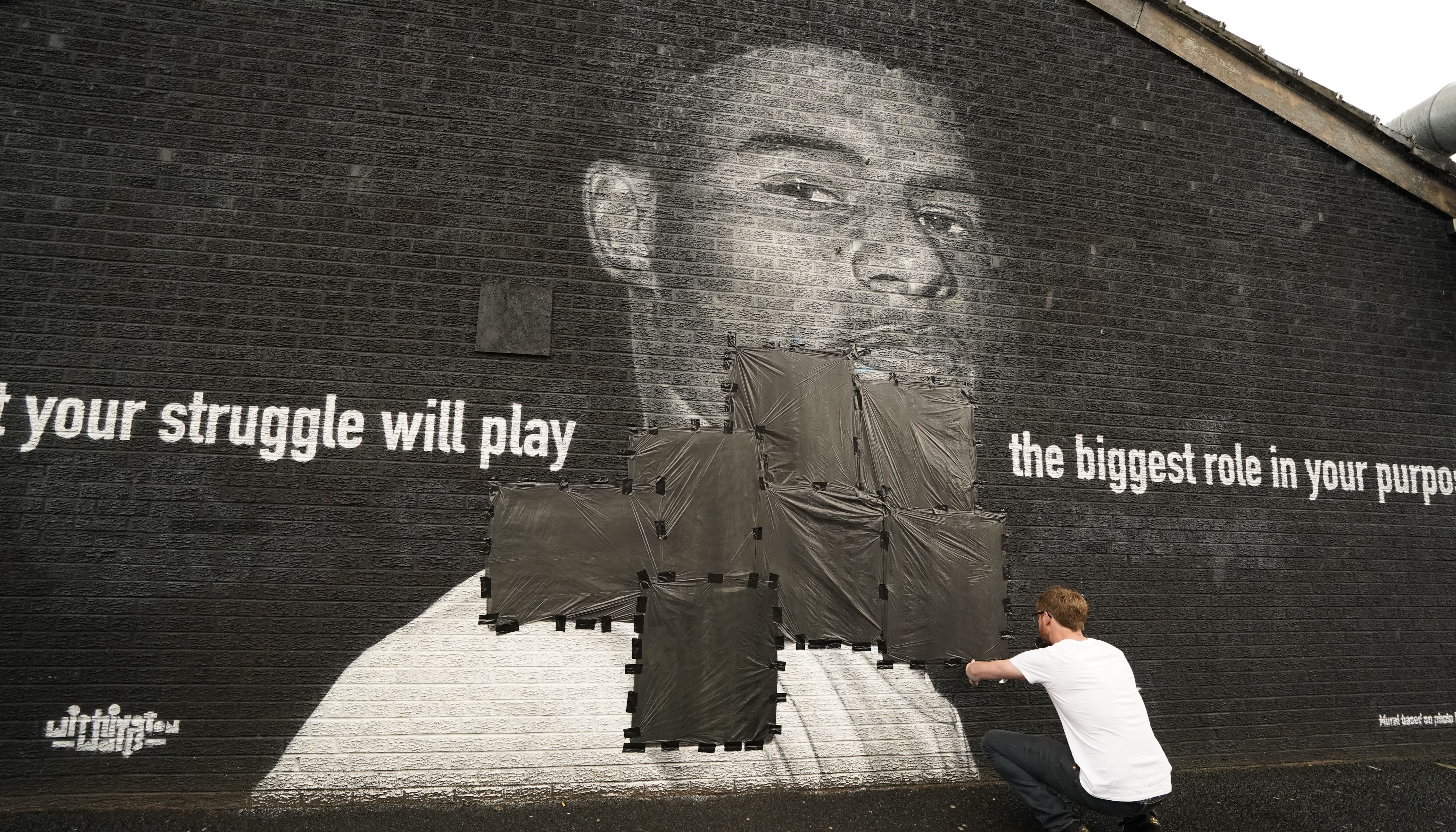 Ed Wellard tapes bin liners across offensive wording on the mural of Manchester United striker and England player Marcus Rashford on the wall of the Coffee House Cafe on Copson Street.