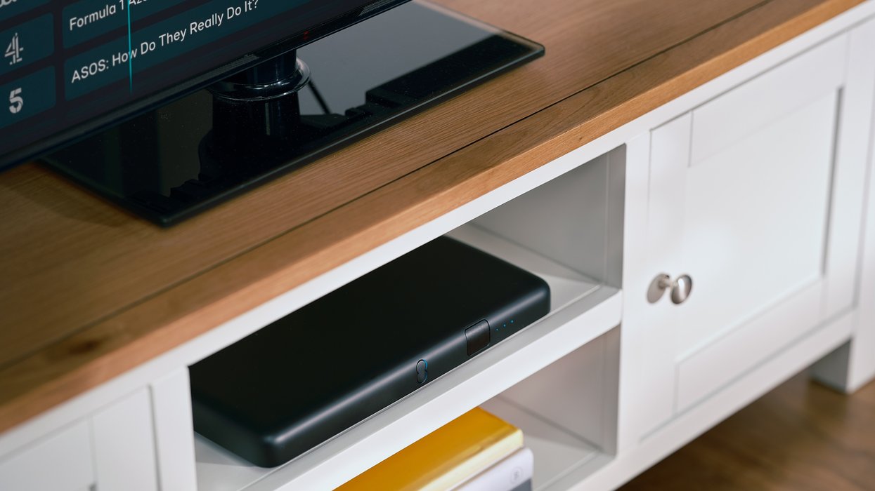 ee tv box pro pictured in a media unit with a flatscreen tv showing the tv guide