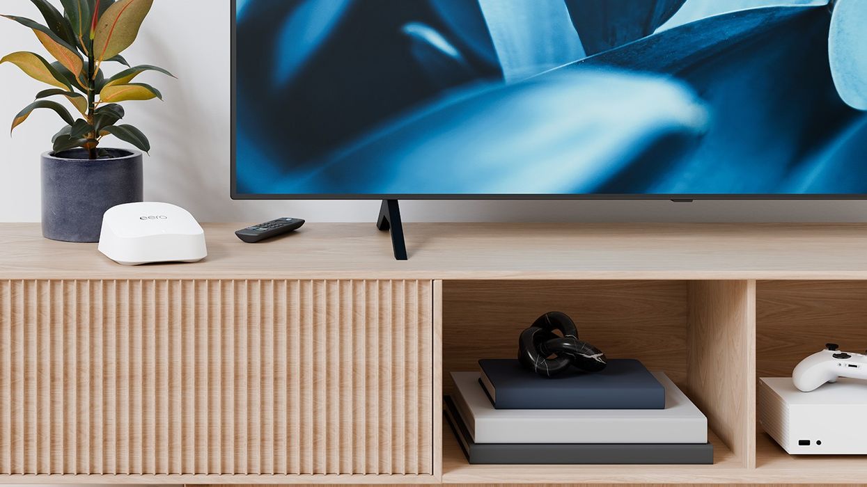 Eero 7 wireless router pictured on a table next to a television with a fire tv remote control and xbox series s