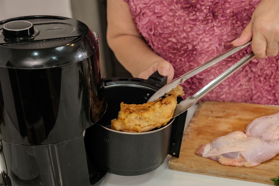 Elderly woman cooking with hot air fryer in the kitchen