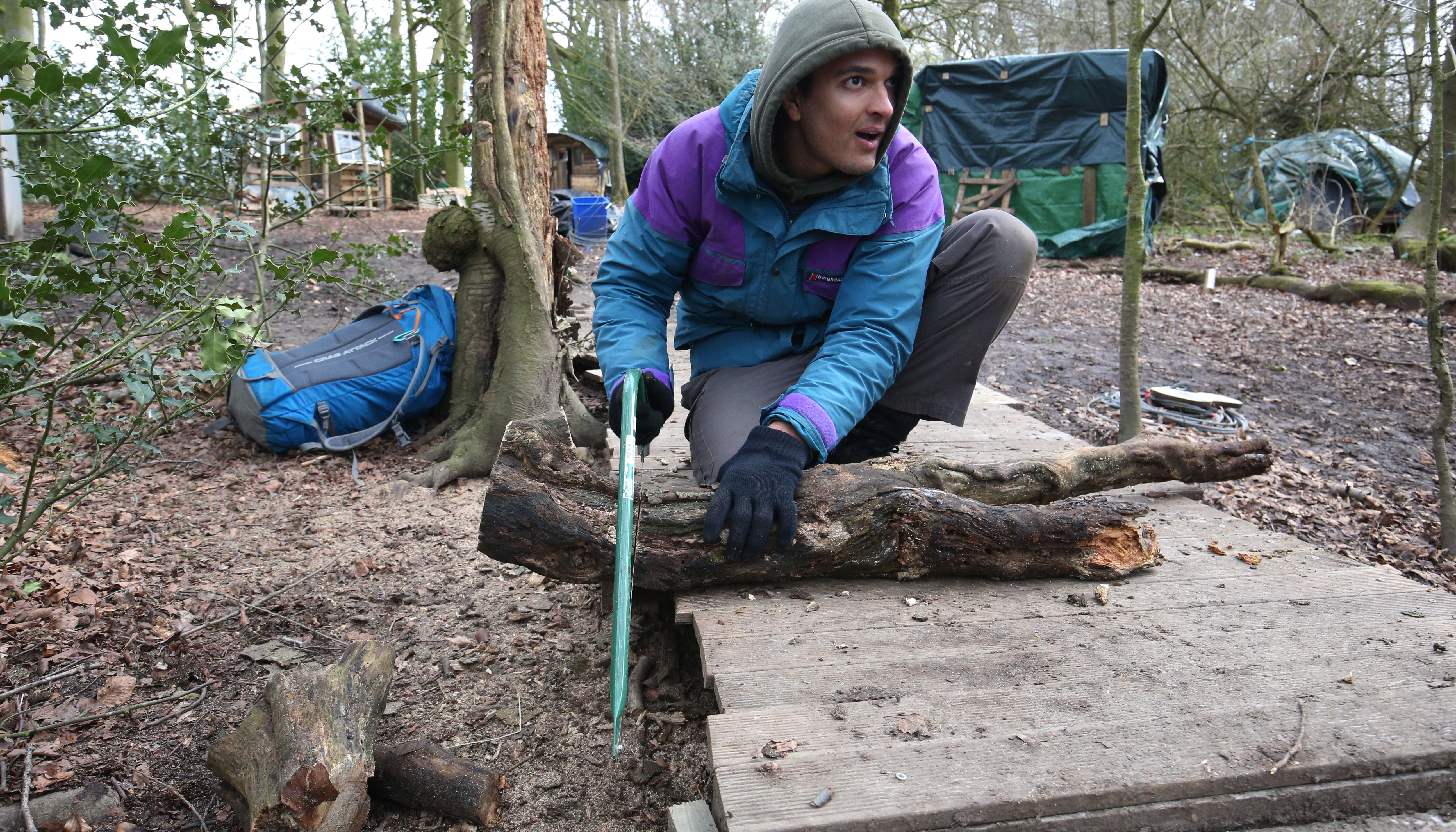 Environmental activist Xavier Gonzalez-Trimmer saws wood for fuel at a protest camp in Jones' Hill Wood, near Aylesbury Vale in Buckinghamshire, in March 2021