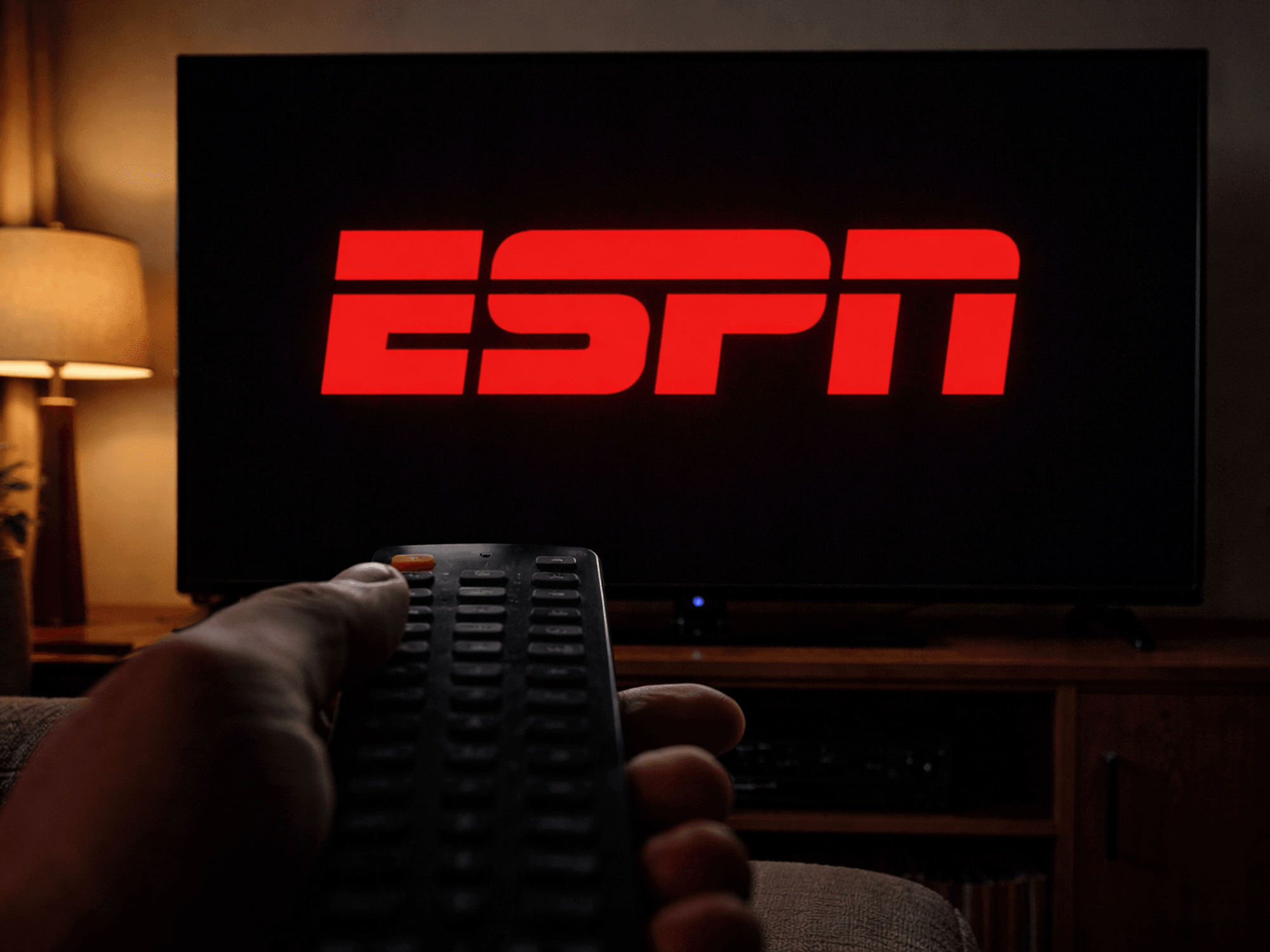 ESPN logo on TV with hand holding remote