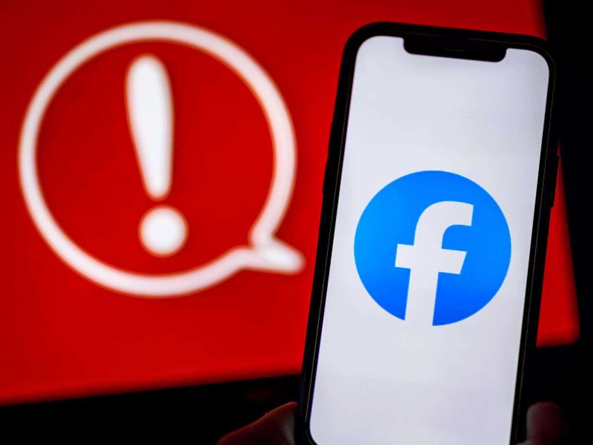 Facebook logo on mobile in front of red warning symbol