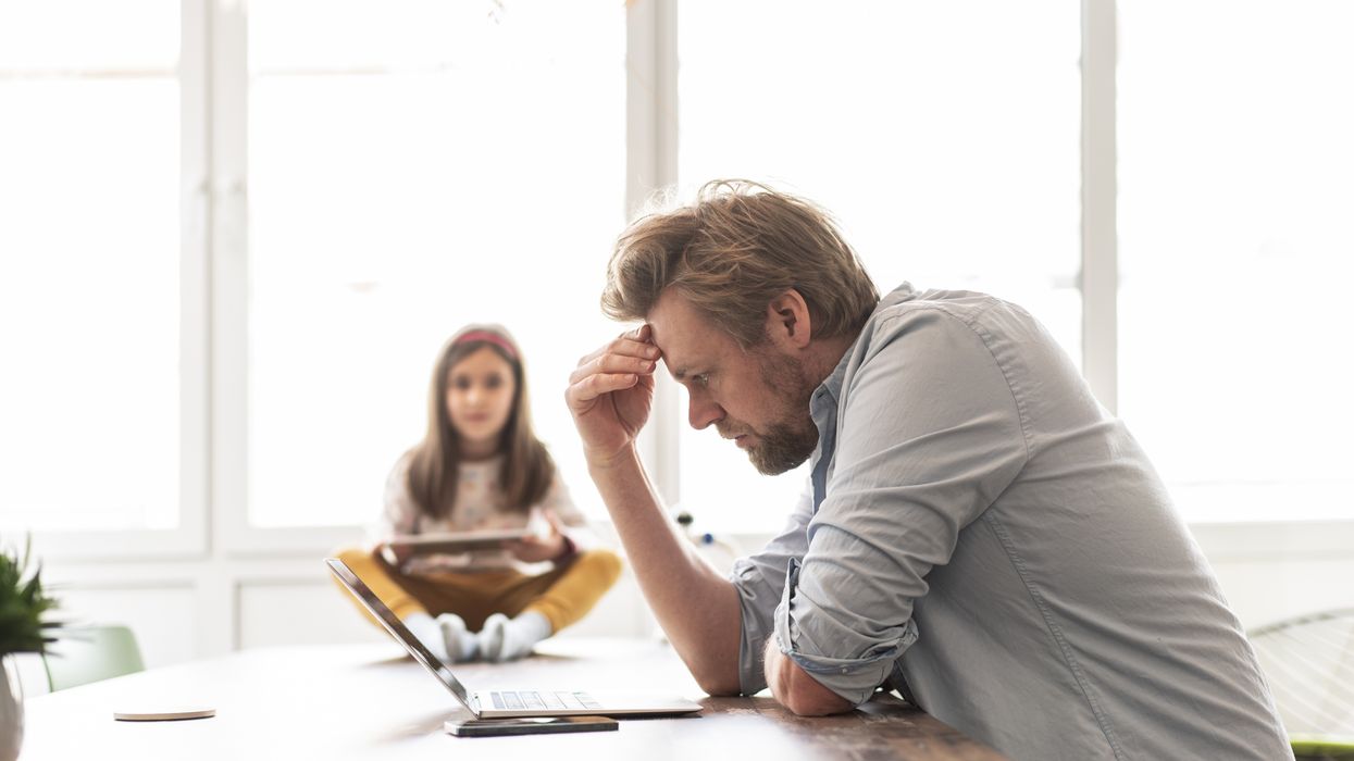 Father looks at laptop with daughter in background