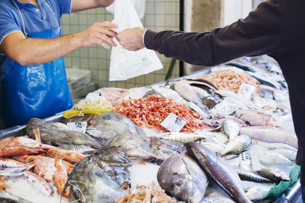 Fish market with all the fish laid out on ice as a man accepts a bag from a market seller