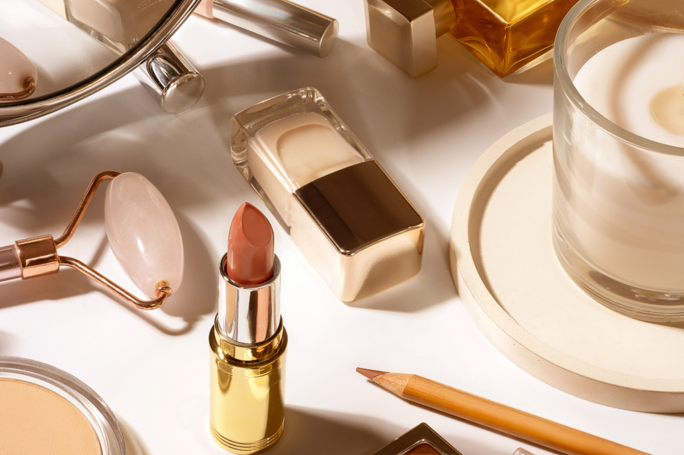 Foundation, jade roller, red lipstick and a candle laid out on a white surface