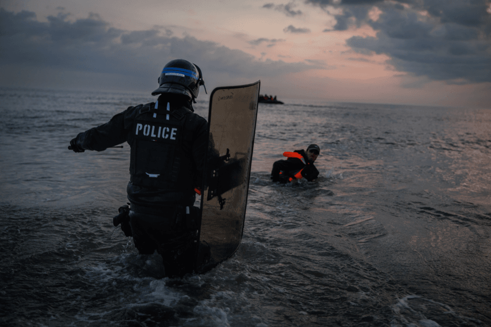 French Police enter the water to try and stop migrants boarding small boats that had come to collect them from further down the coastline on June 13, 2025 in Gravelines, France.