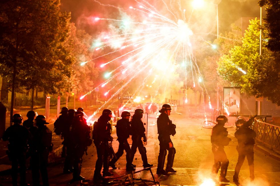 French police stand in position as fireworks go off during clashes with youth