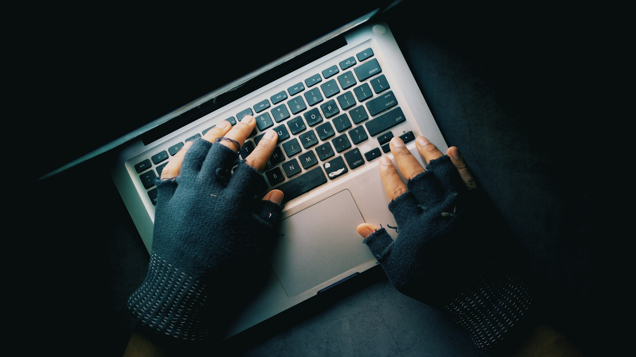 gloved hands pictured on the keyboard of a laptop typing in the dark