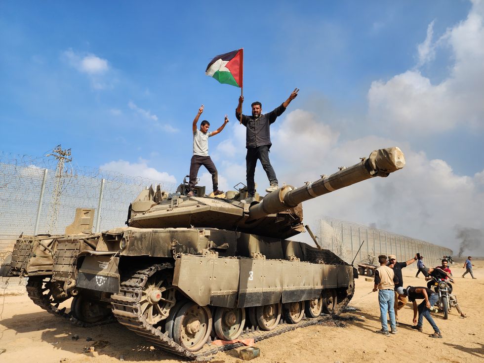 Hamas' armed wing, the Izz ad-Din al-Qassam Brigades hold a Palestinian flag as they destroy a tank of Israeli forces in Gaza City