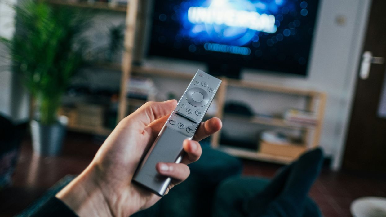 hand holding a remote control with a television in the background showing a film