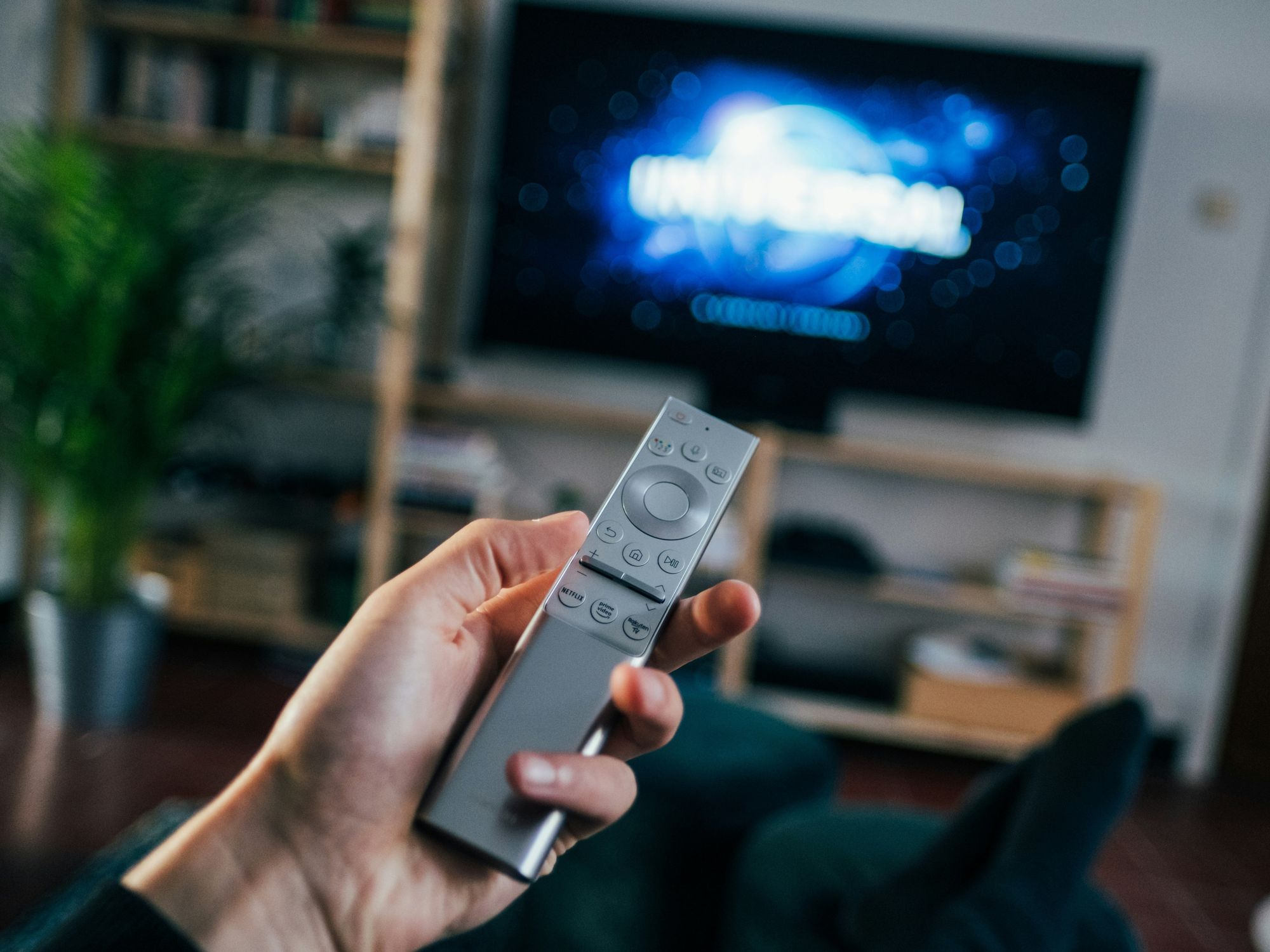 hand holding a remote control with a television in the background showing a film