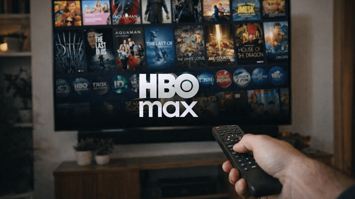 Hand holding a remote in front of TV screen displaying HBO Max logo