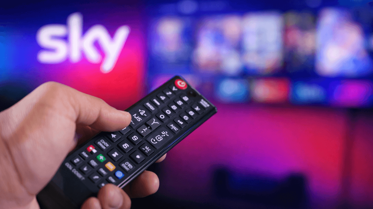 Hand holding a TV remote in front of a TV and Sky logo