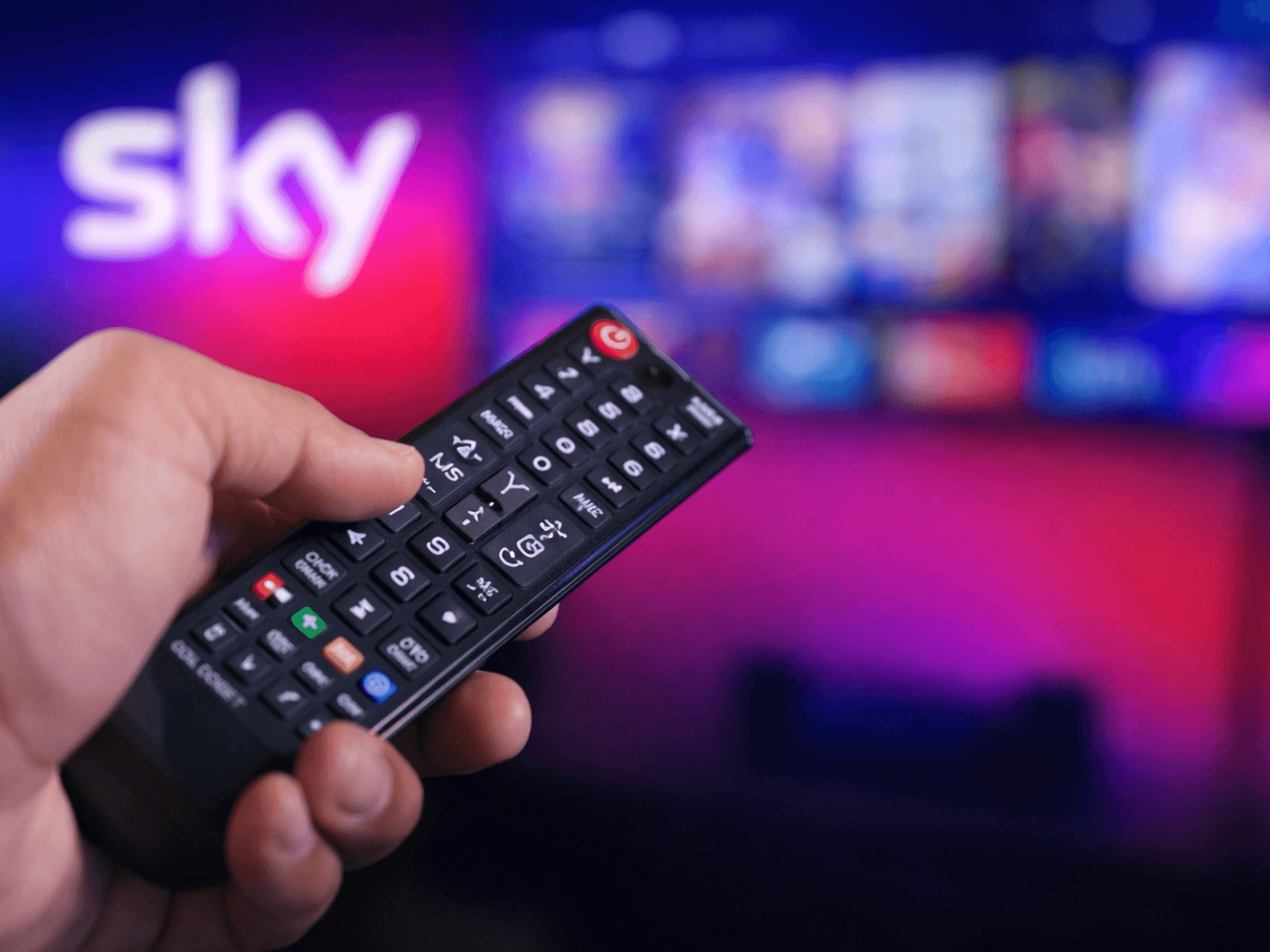 Hand holding a TV remote in front of a TV and Sky logo