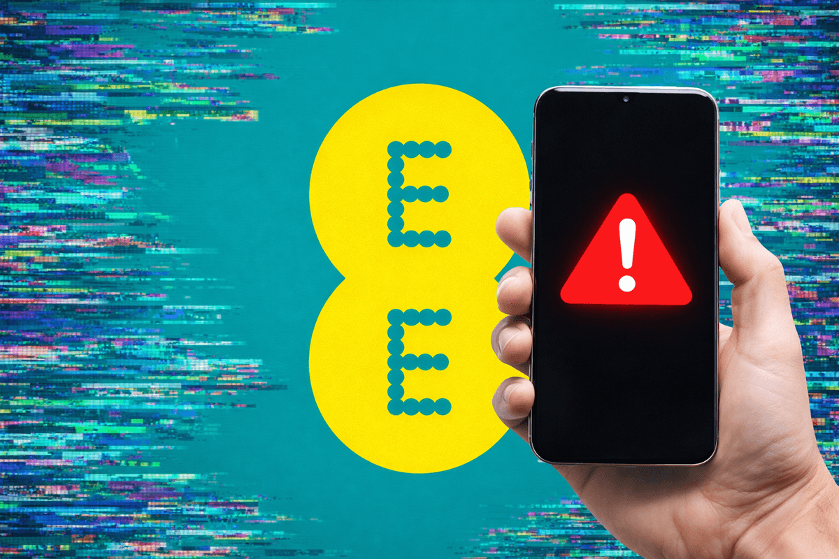 Hand holding mobile with warning symbol in front of EE logo